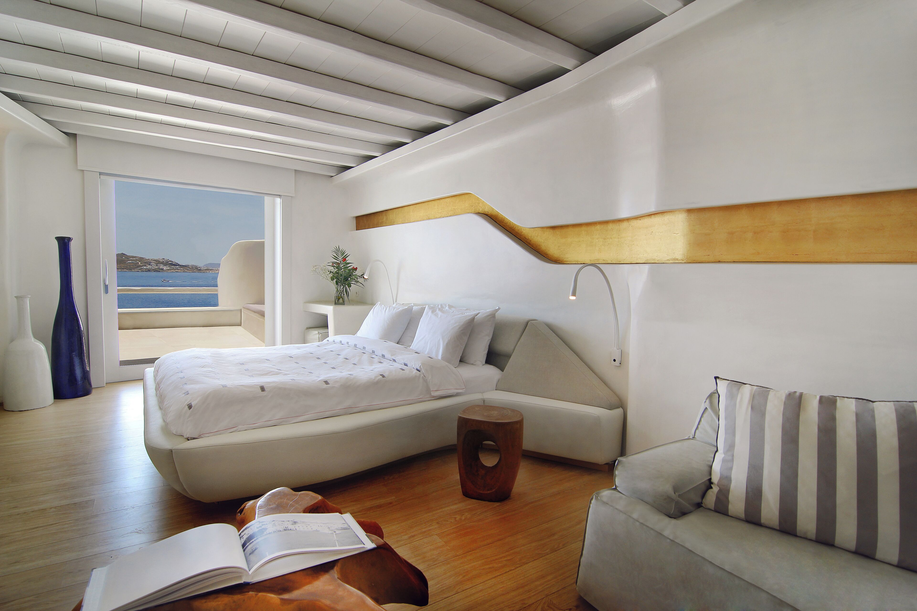 Une chambre à coucher moderne avec un lit, un canapé, un tabouret en bois et une vue sur la mer.