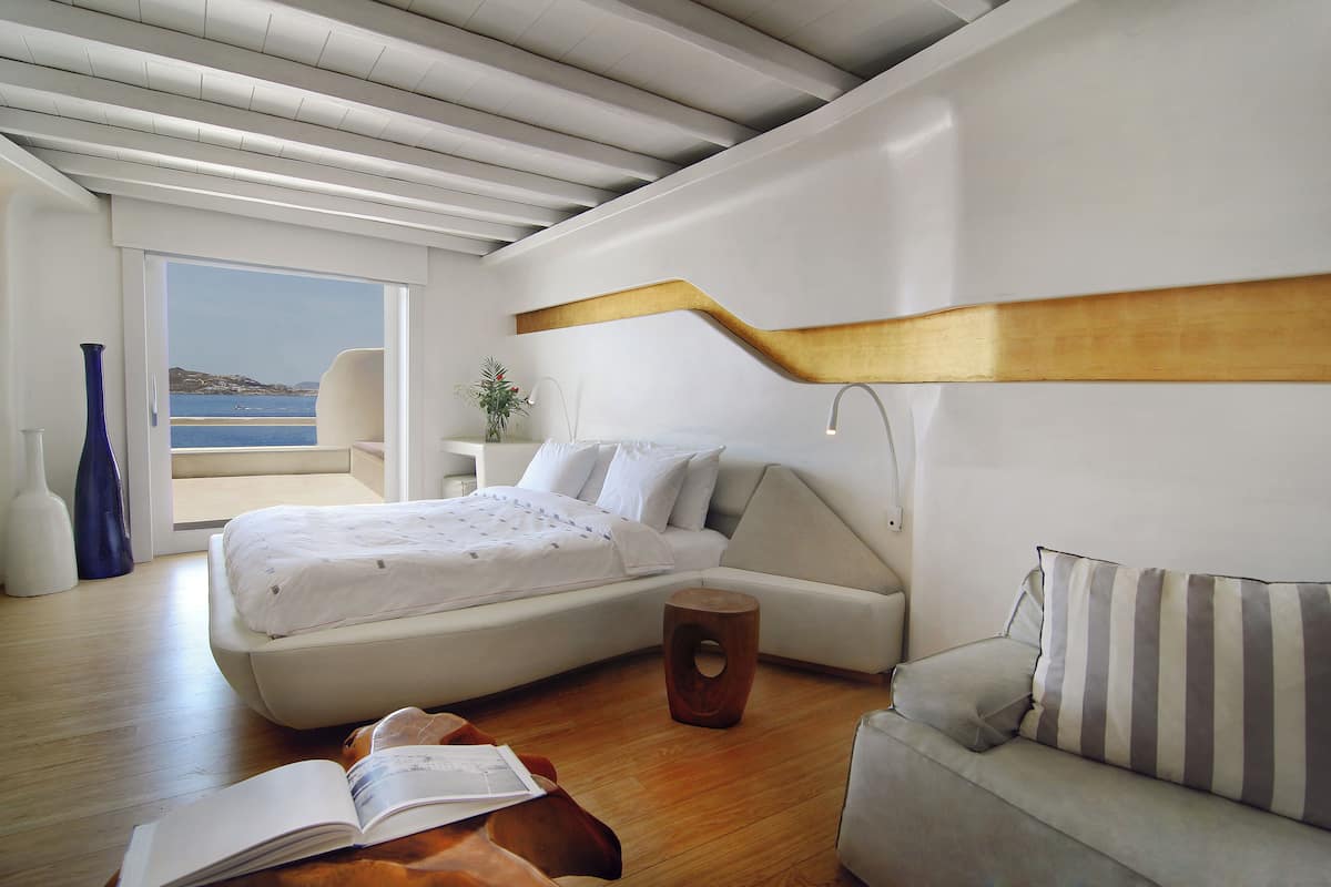 Une chambre à coucher moderne avec un lit, un canapé, un tabouret en bois et une vue sur la mer.