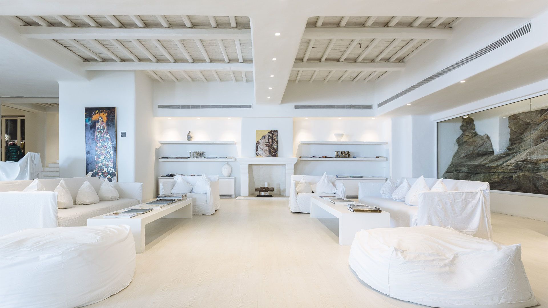 A spacious, modern living room with white sofas, a fireplace, and artwork on the walls.