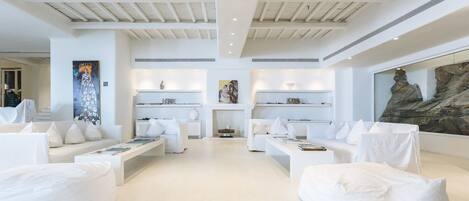 A spacious, modern living room with white sofas, a fireplace, and artwork on the walls.