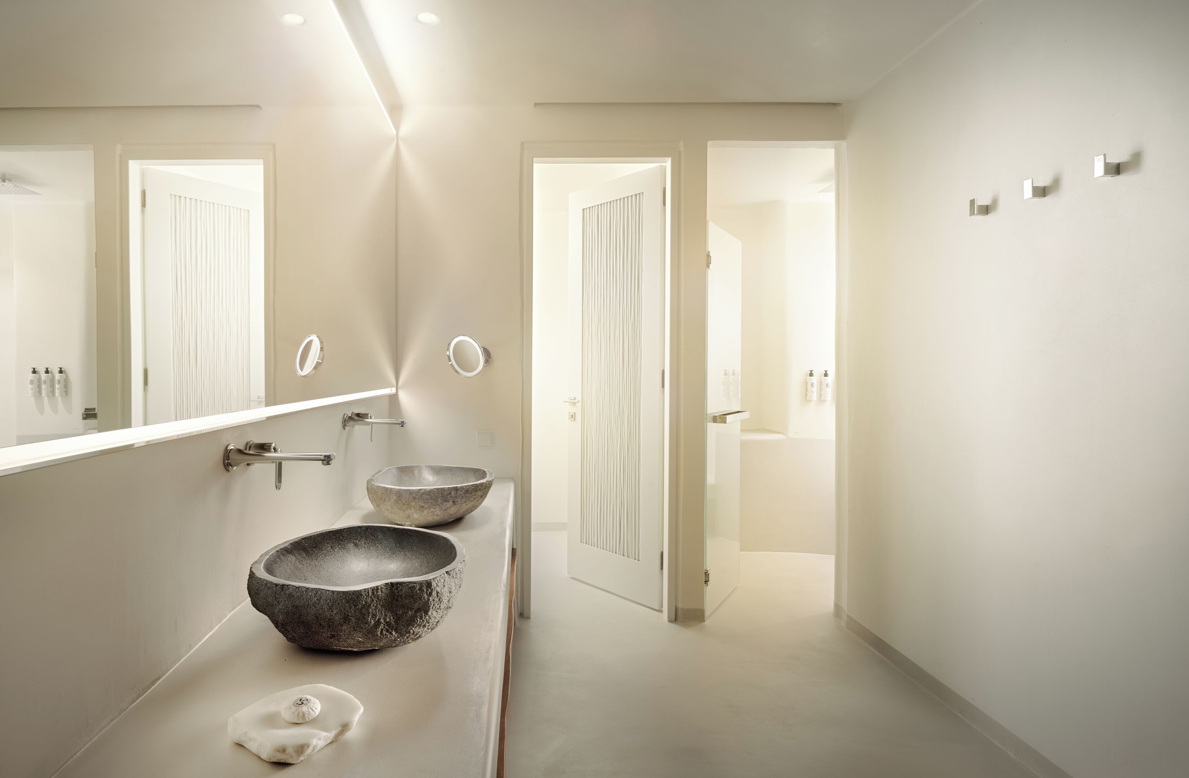 A modern bathroom with two large stone sinks, a large mirror, and a walk-in shower.