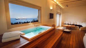 A modern bathroom with a large bathtub, wooden flooring, and a view of a cruise ship. - CAVO TAGOO MYKONOS (Mykonos)