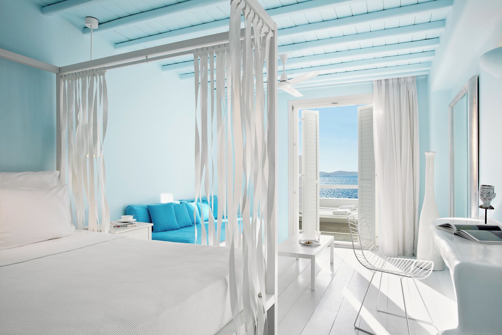 Une chambre avec un grand lit, un canapé bleu, un bureau avec une chaise et une vue sur la mer.