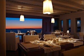 A restaurant with tables set for dining, featuring a view of the sunset over the sea.