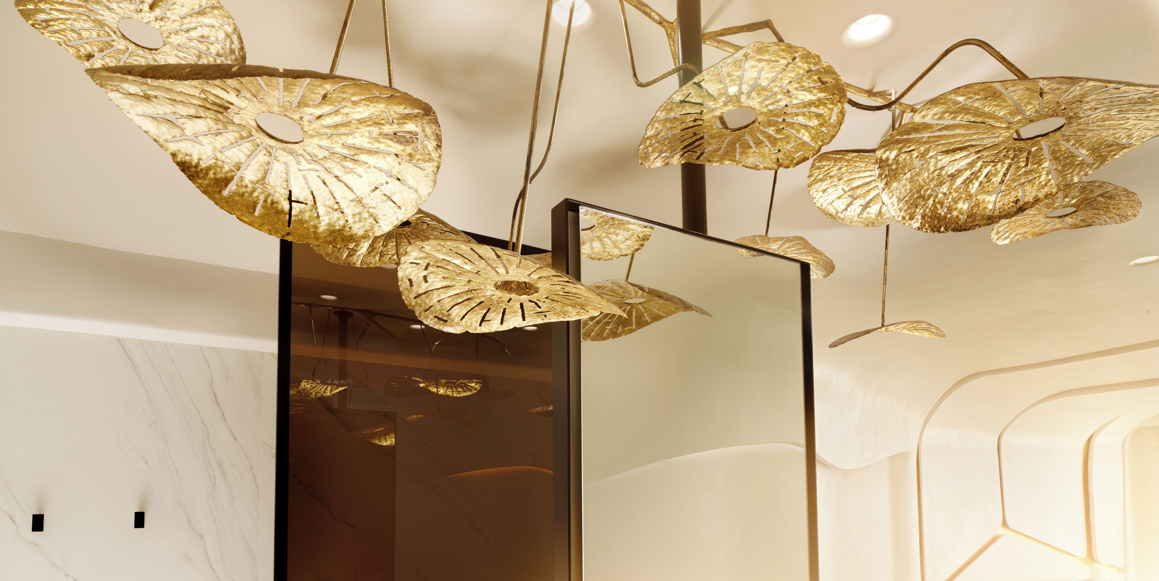 A modern interior with a reflective surface and decorative golden leaf-shaped light fixtures.