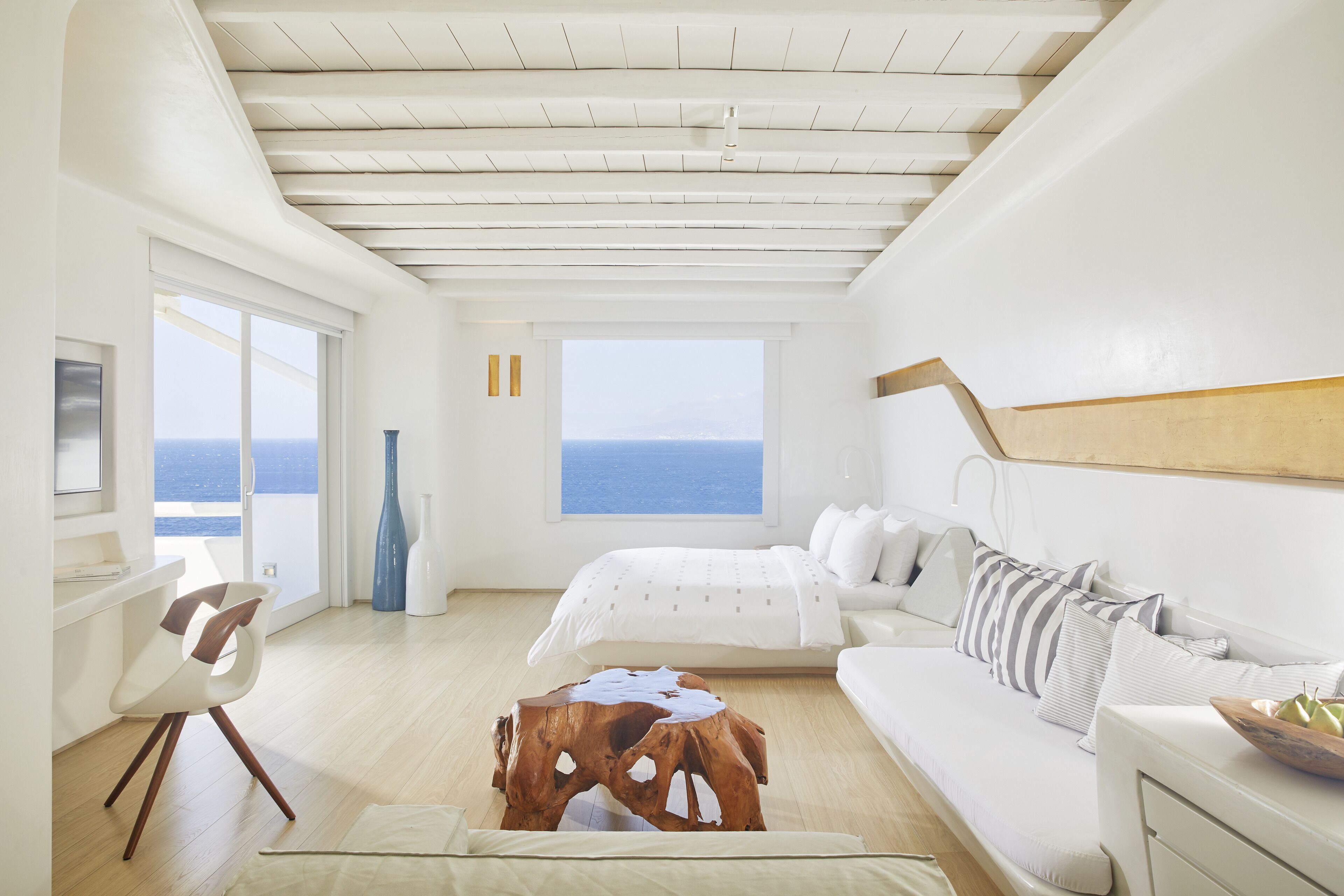 A modern bedroom with a large window, a bed, a sofa, and a wooden coffee table.