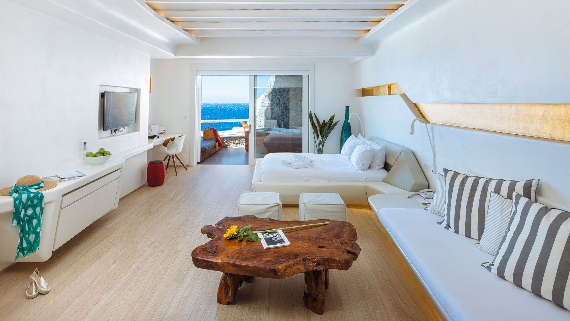 Un salón moderno y bien iluminado con una mesa de centro de madera, un sofá blanco y un televisor en la pared izquierda.