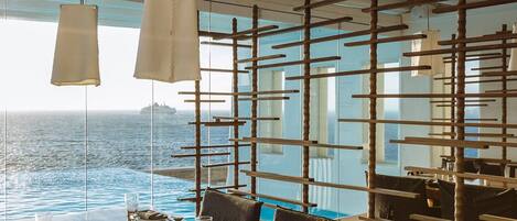 A dining area with a wooden table set for two, overlooking a pool and the ocean.