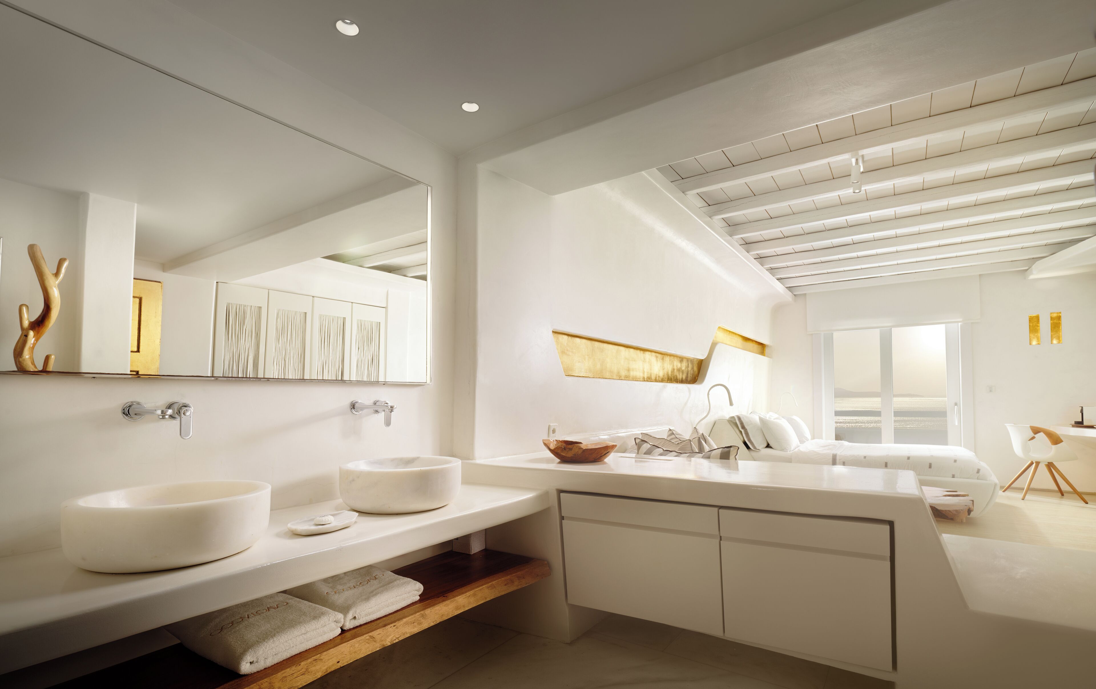 A modern bathroom with a large mirror, two sinks, a bathtub, and a shower. There is a wooden shelf with towels and a window providing a view of the outdoors.