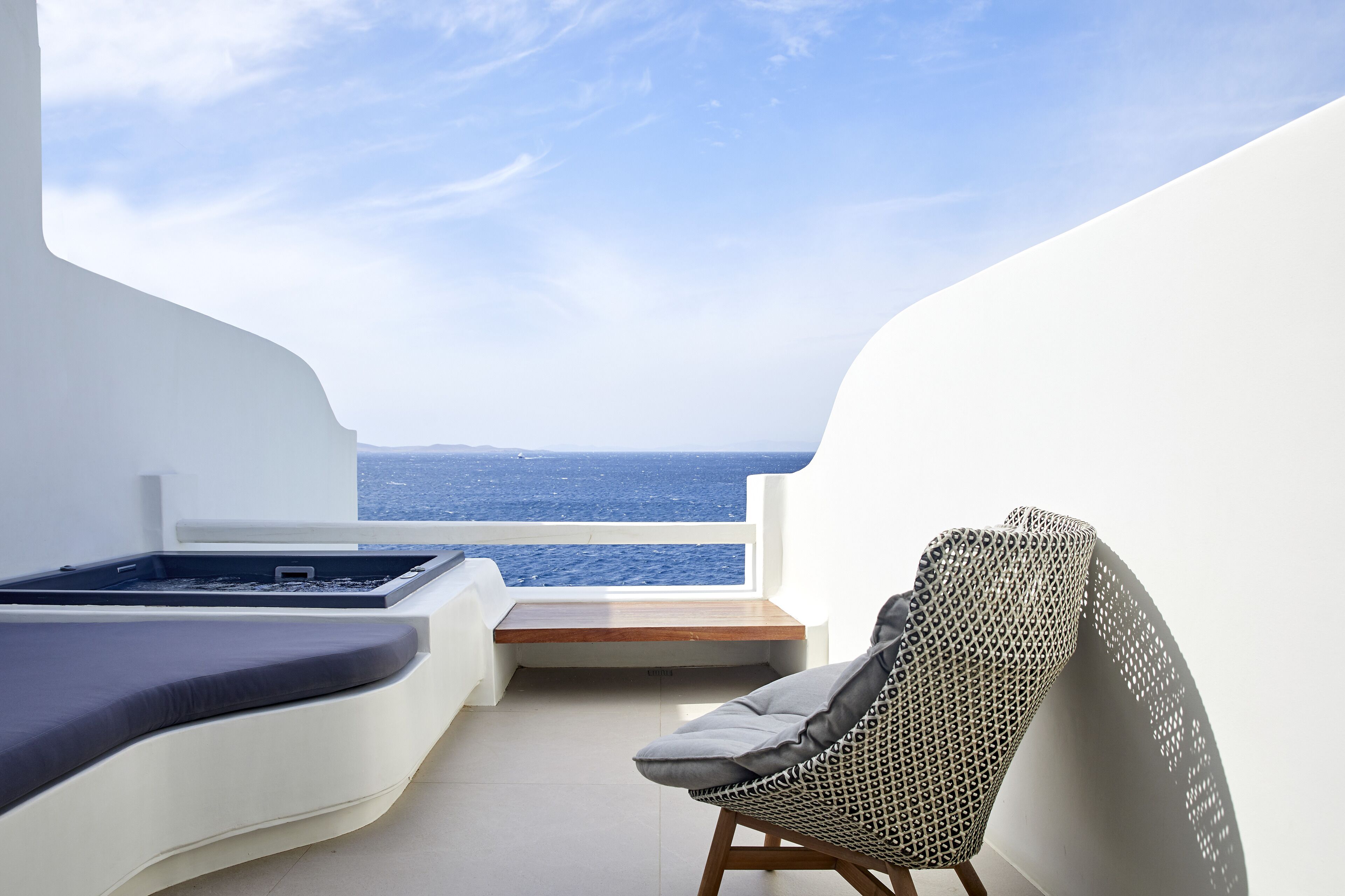 A balcony with a view of the sea, a lounge chair, and a small seating area.
