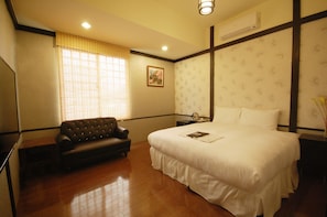 A hotel room with a large bed, a sofa, a bedside table, and a window with blinds. - Hananoi Bed and Breakfast (Hengchun)