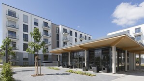 A modern building with multiple balconies, a covered outdoor seating area, and a landscaped courtyard.