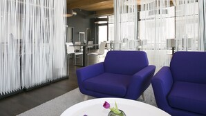 A modern office space with two blue chairs, a white table with a vase and a card, and a white, vertical, perforated partition.