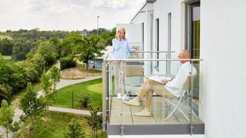 A modern building with a balcony overlooking a landscaped garden and a golf course.