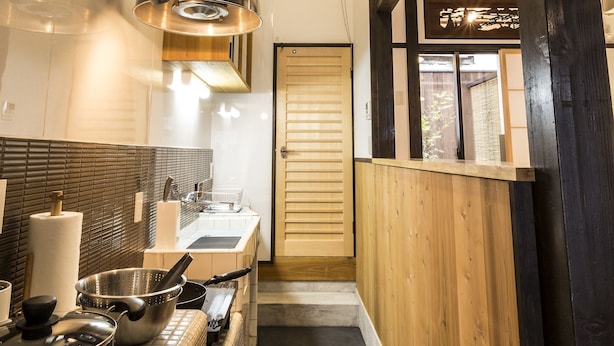 Una cocina estrecha con salpicadero de azulejos, un lavamanos de acero inoxidable y una encimera de madera. Se aprecia una ventana grande con vistas al exterior.