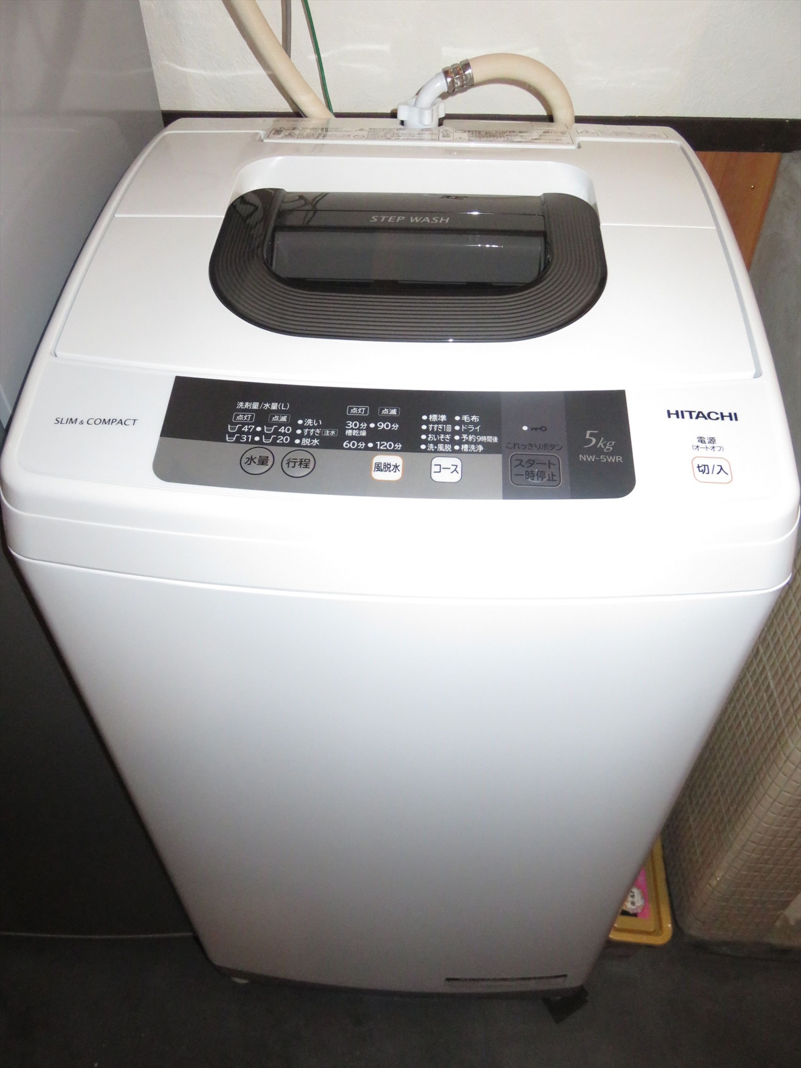 A white, compact washing machine with a control panel displaying various settings and a 5kg capacity label.