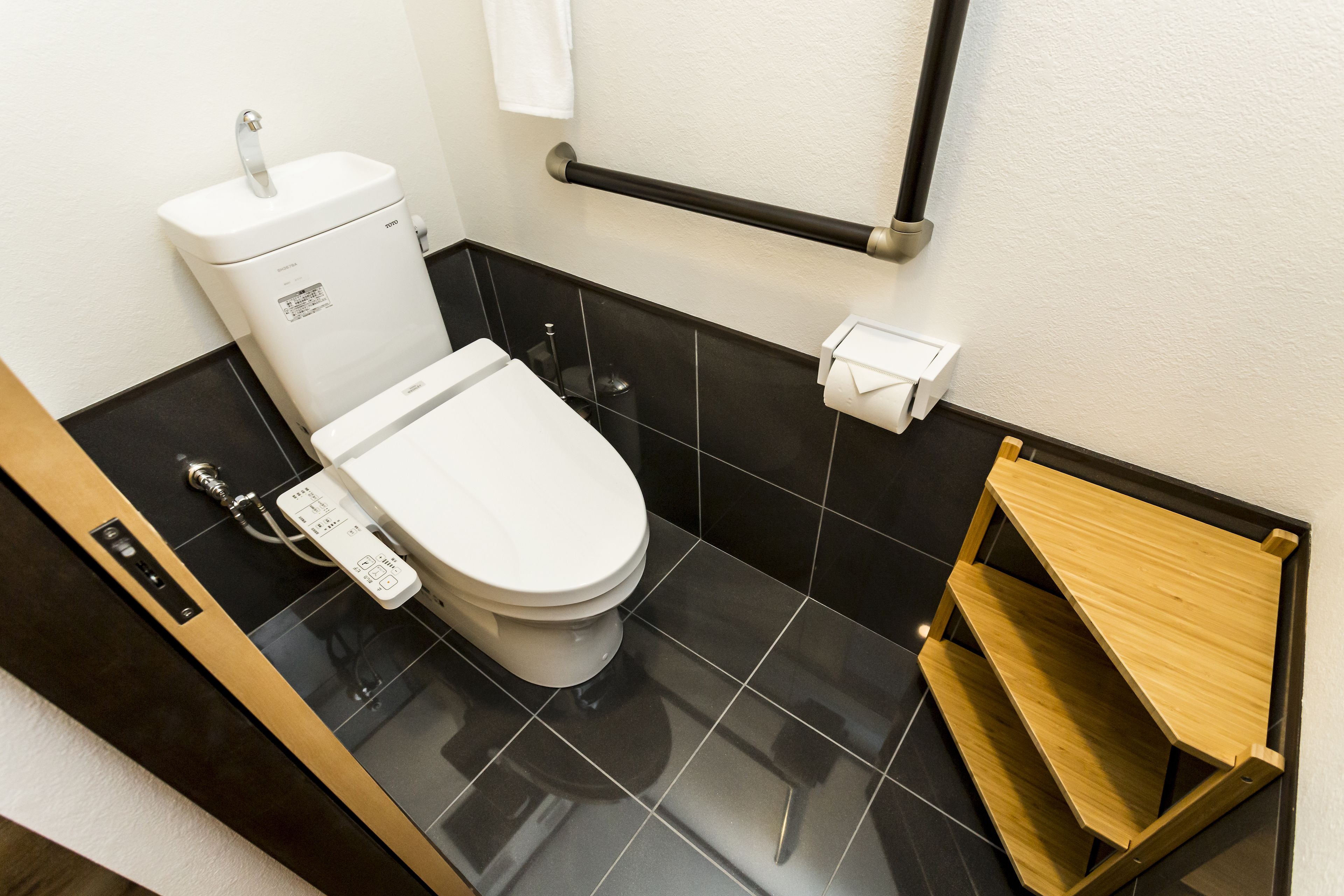 Un baño moderno con inodoro, bidé, secamanos y un estante de madera.