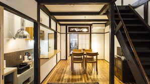 Un interior japonés tradicional con suelo de madera, una zona de comedor con dos sillas, una cocina con estufa y una escalera.