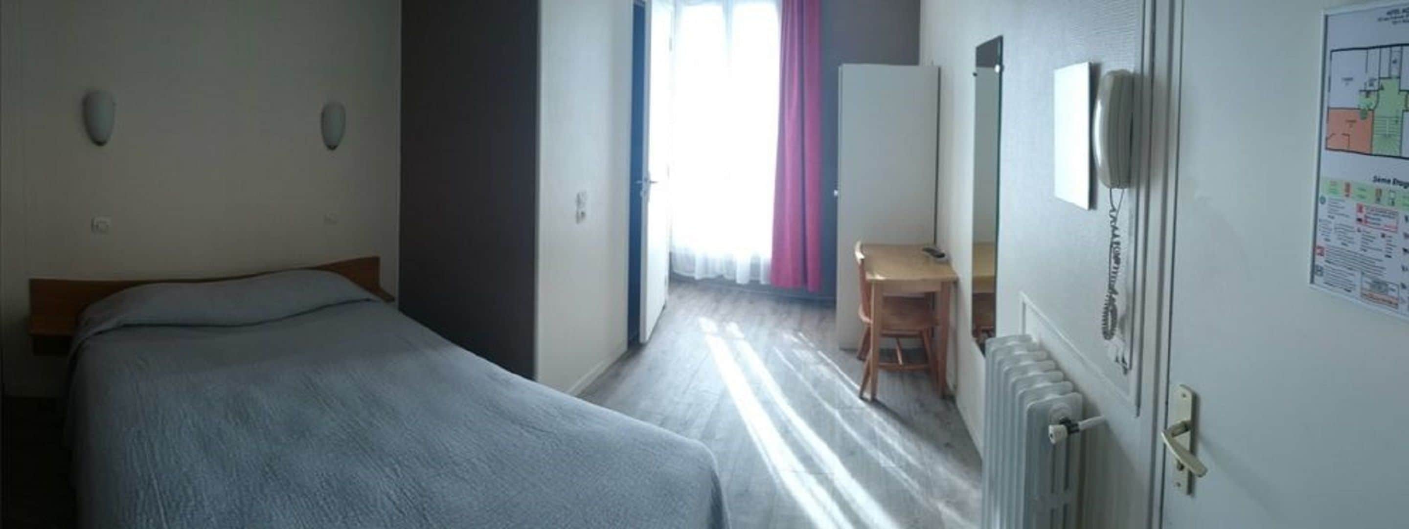 A hotel room with a bed, a desk, and a radiator.