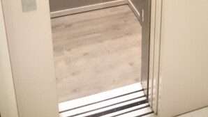 An elevator with metallic walls and a door, featuring a control panel with a button and a small display. - Acacia Hotel (Paris)