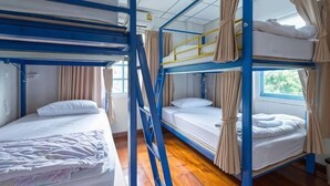 A bunk bed room with curtains, wooden flooring, and a window.