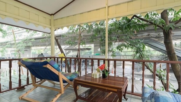 A covered balcony with a wooden table, a blue cushioned chair, and a wooden bench.