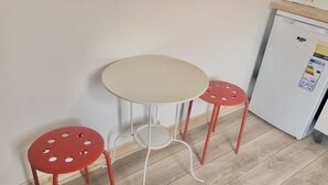 Une petite cuisine équipée avec un réfrigérateur blanc, une table beige et deux chaises rouges.
