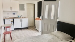 Une pièce de taille modeste comprenant un lit, une petite kitchenette et une porte donnant sur une autre pièce.