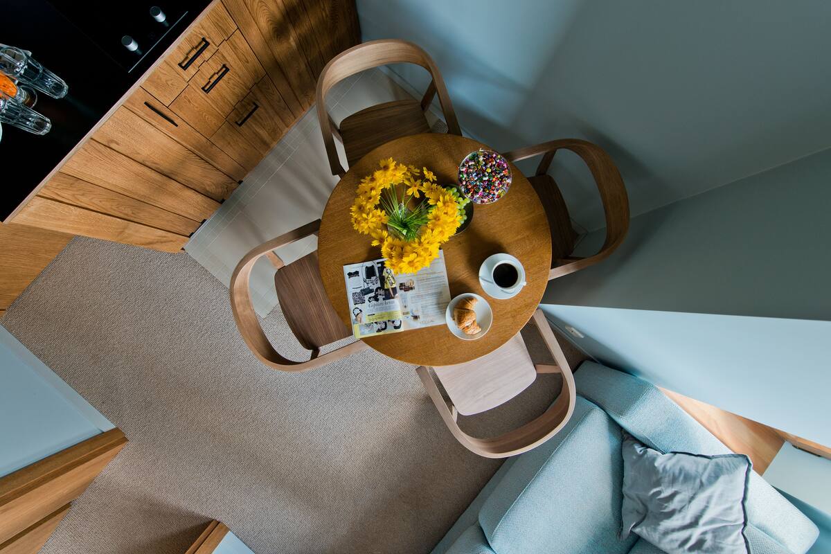 Overzicht van een eetgedeelte met een houten tafel, stoelen, een vaas met gele bloemen, een schaal met kleurrijke snoepjes, een kop koffie en een menukaart.