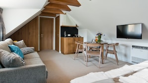 Un dormitorio estilo loft moderno con techo inclinado, cocina integrada, televisor de pantalla plana y una zona de estar acogedora con sofá y sillones.