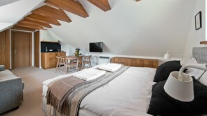Un dormitorio moderno con techo estilo loft, una cama con cubrecama blanco, un escritorio con silla y un televisor montado en la pared.