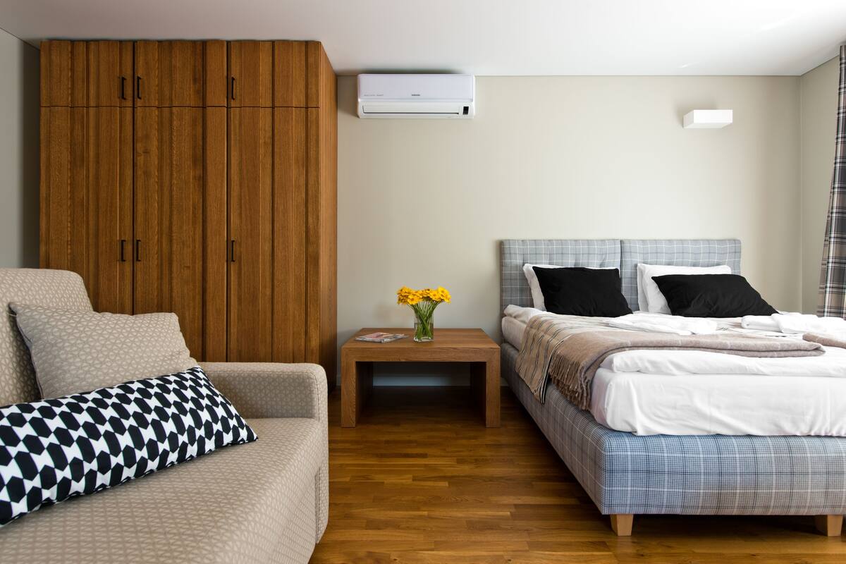 Een hotelkamer met een bed, een slaapbank, een houten garderobe, een nachtkastje met een bloevas en een airconditioning.