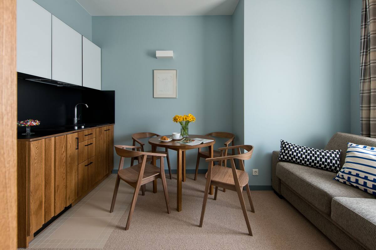 Een compacte woonruimte met een kitchenette, een eettafel met stoelen en een bank met gestreepte kussens.