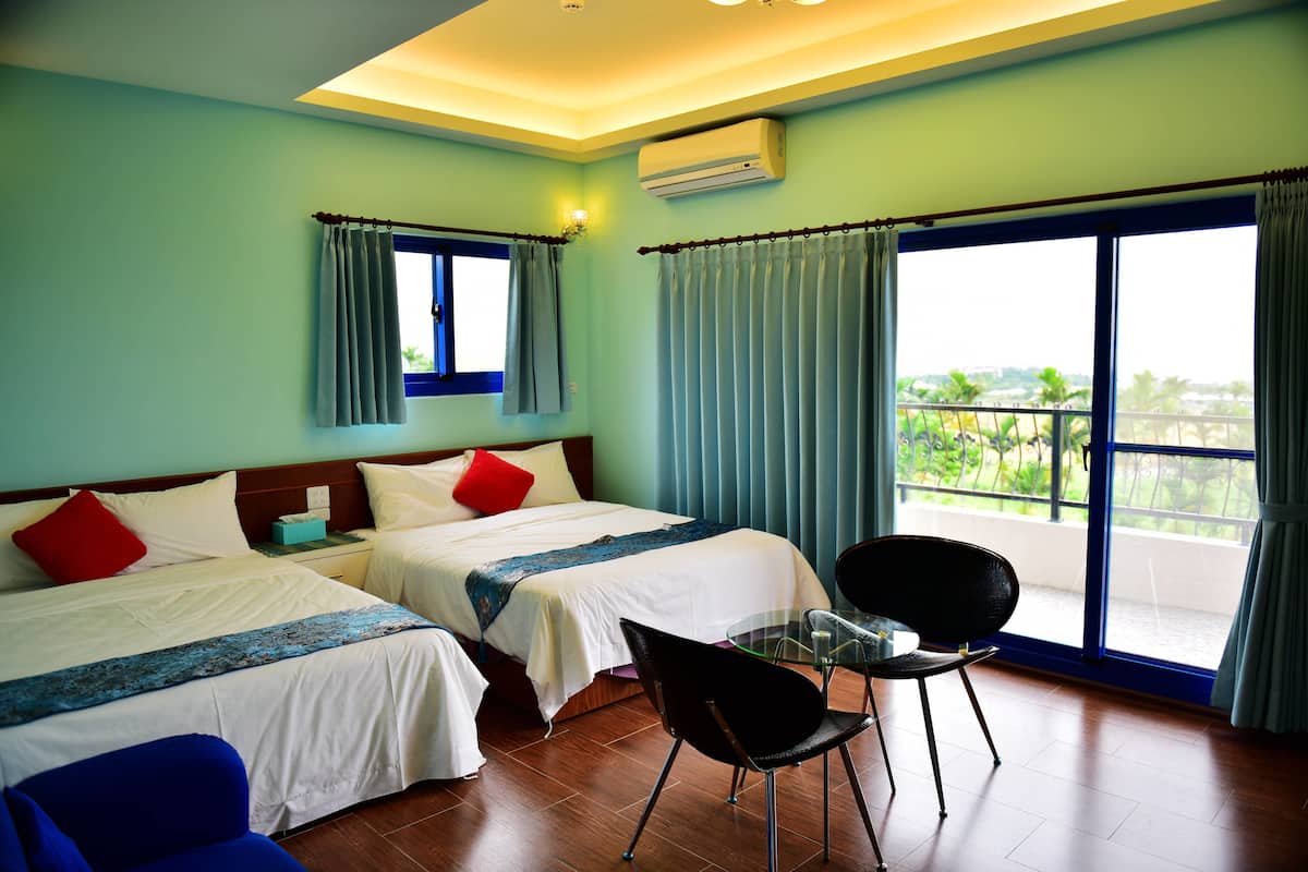 A hotel room with two beds, a balcony with a view, and a small table with a chair.