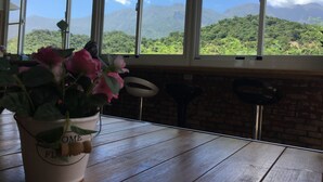 A wooden table with a potted plant and a view of a mountainous landscape through large windows. - Happiness House (Chenggong)