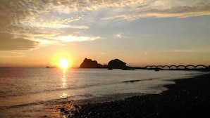 A sunset over a beach with a bridge in the distance. - Happiness House (Chenggong)