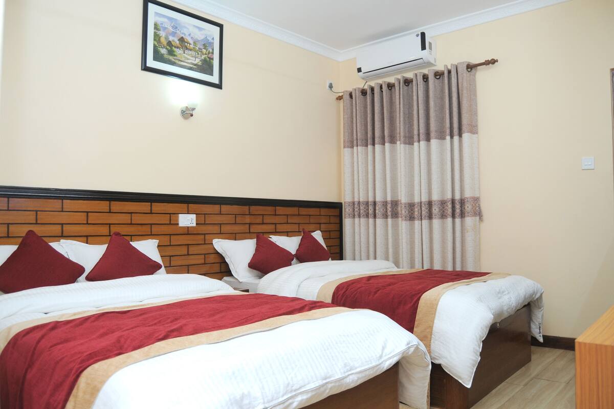 A hotel room with two beds, each with red and white bedding, a brick headboard, a picture on the wall, and an air conditioning unit.