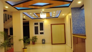 A hotel lobby with a skylight ceiling, a chandelier, potted plants, and a wooden reception desk. - Hotel Bagmati (Kathmandu)