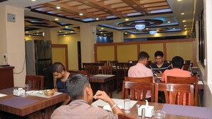 A restaurant with wooden tables and chairs, a chandelier, and a modern ceiling design. - Hotel Bagmati (Kathmandu)