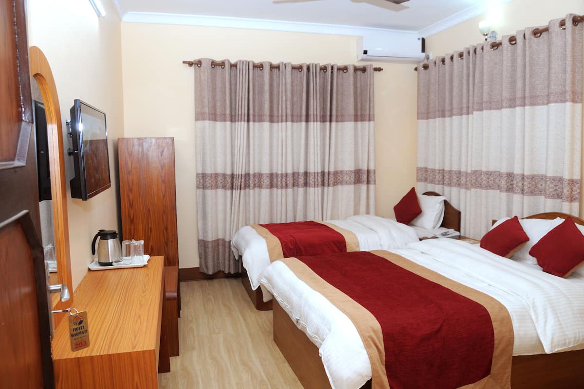 A hotel room with two beds, a wooden desk with a coffee maker, and curtains.