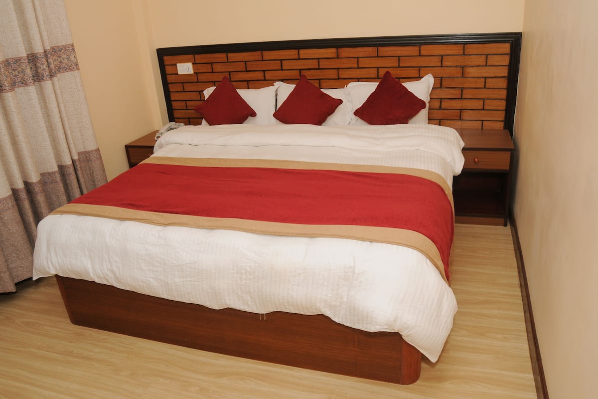 A bed with a wooden headboard, red and white bedding, and a wooden nightstand beside it.