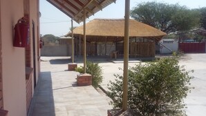 Un espacio al aire libre cubierto con una estructura de techo de paja, un extintor de incendios montado en una pared y una pequeña maceta de ladrillo con un arbusto.