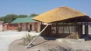 Una estructura de techo de paja con valla de madera, un edificio de techo verde y una planta pequeña en primer plano.