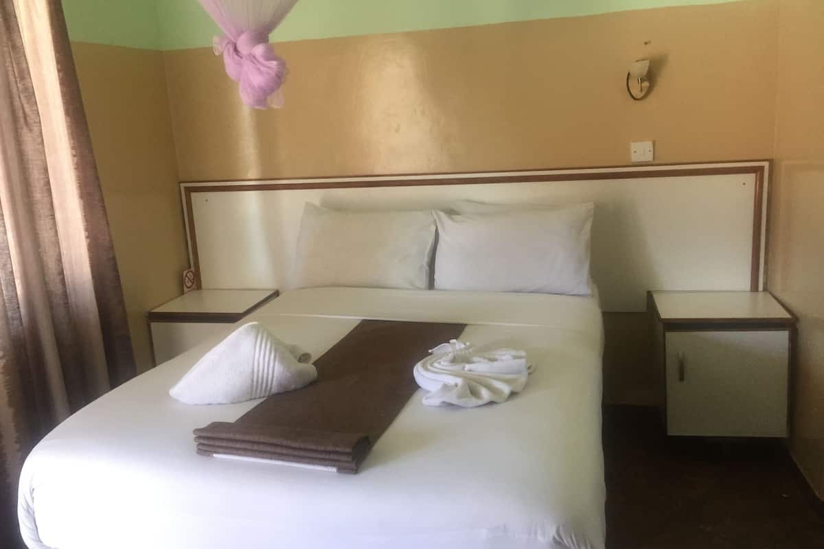 Una cama bien hecha con ropa de cama blanca y marrón, una toalla blanca y un dosel rosa.
