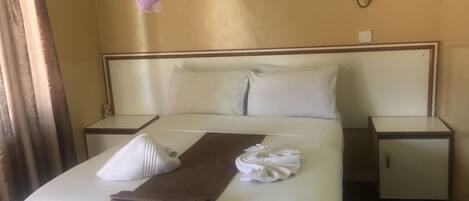 A neatly made bed with white and brown linens, a white towel, and a pink canopy.