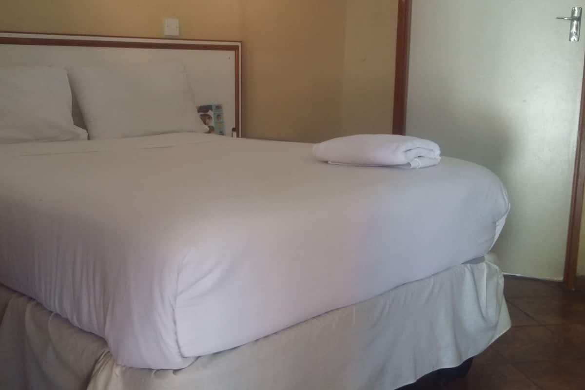 Una cama bien tendida con una toalla blanca doblada en el reposapiés, un cabecero de madera y una puerta a la derecha.