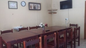 Un comedor con una mesa y sillas de madera, un lavamanos, un reloj, cuadros enmarcados y un televisor fijado a la pared.