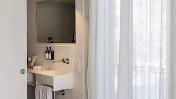 Un baño con un lavamanos blanco, espejo y toallero.