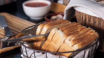 A basket of sliced bread on a kitchen counter with a knife, a bowl of soup, and condiments.