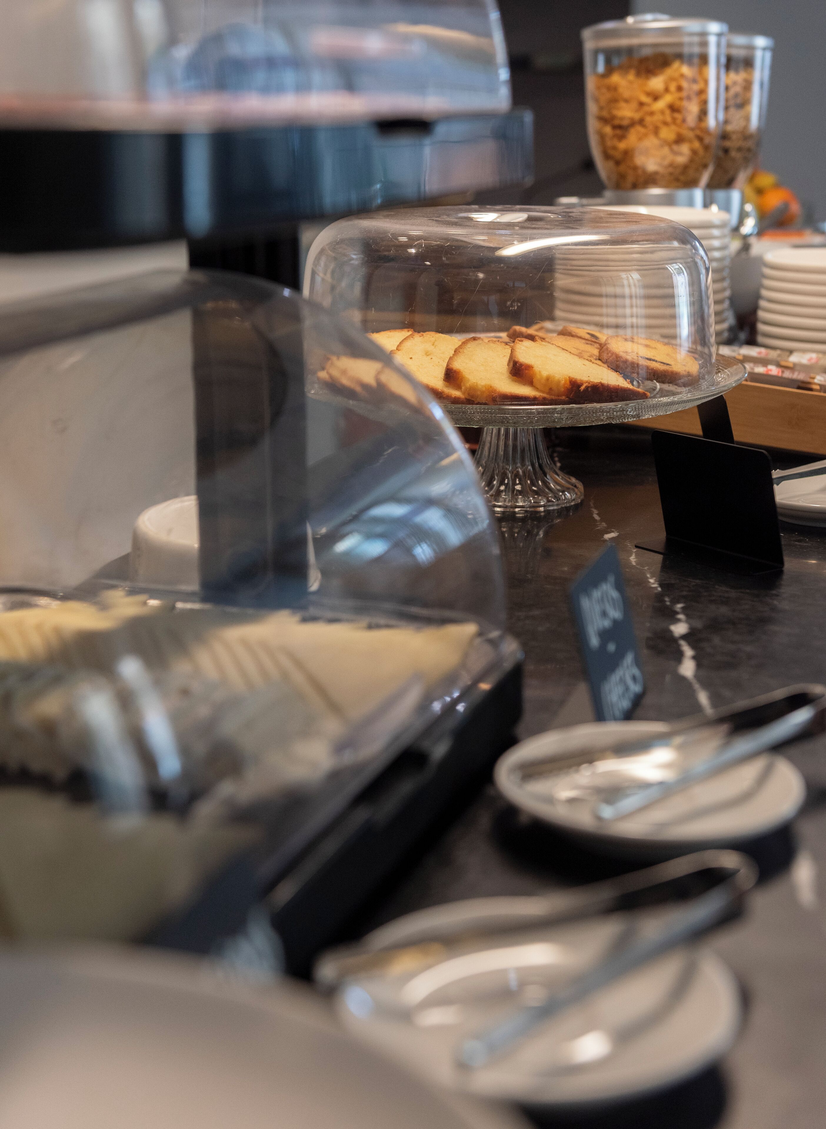 A buffet area with various food items under glass covers, including a cake display and a cereal bowl.